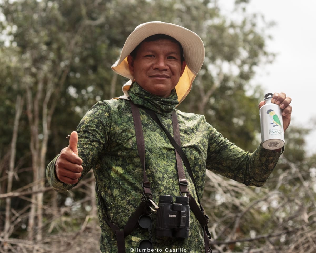 Edgar Noteno Kichwa man wearing birdwatching gear hold water bottle in left hand and thumbs up on his right