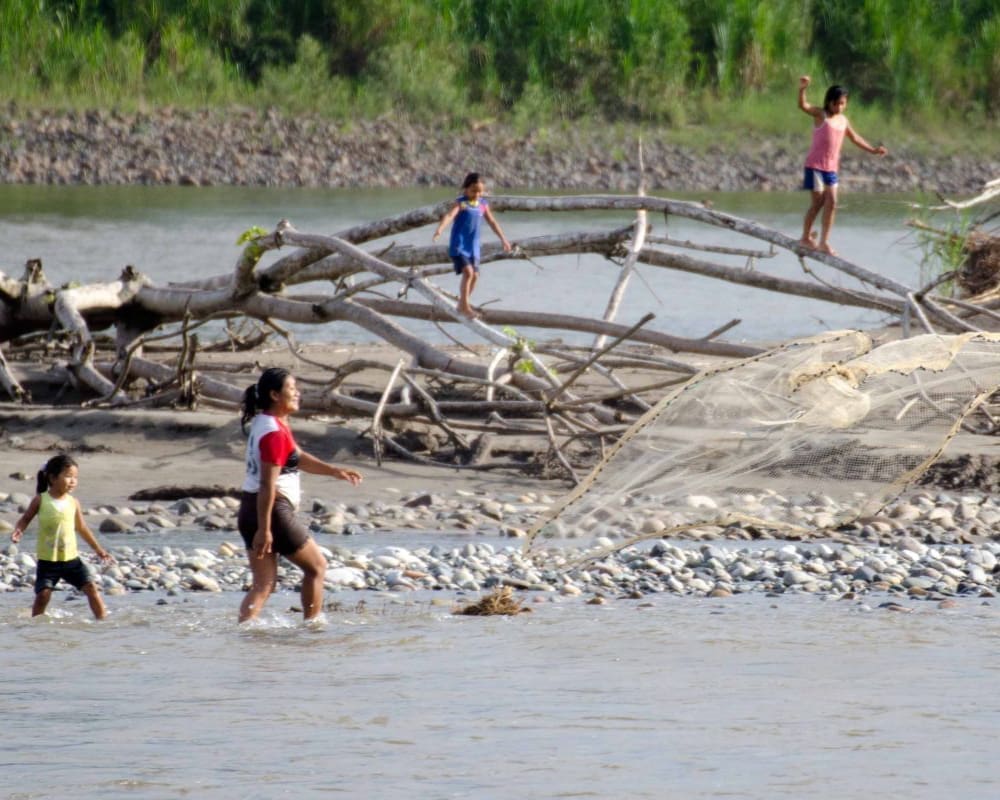 Family fishing along the Napo River | ©Angela Drake, Not Your Average American, LLC woman tosses a weighted fishing net into the river while her children play nearby